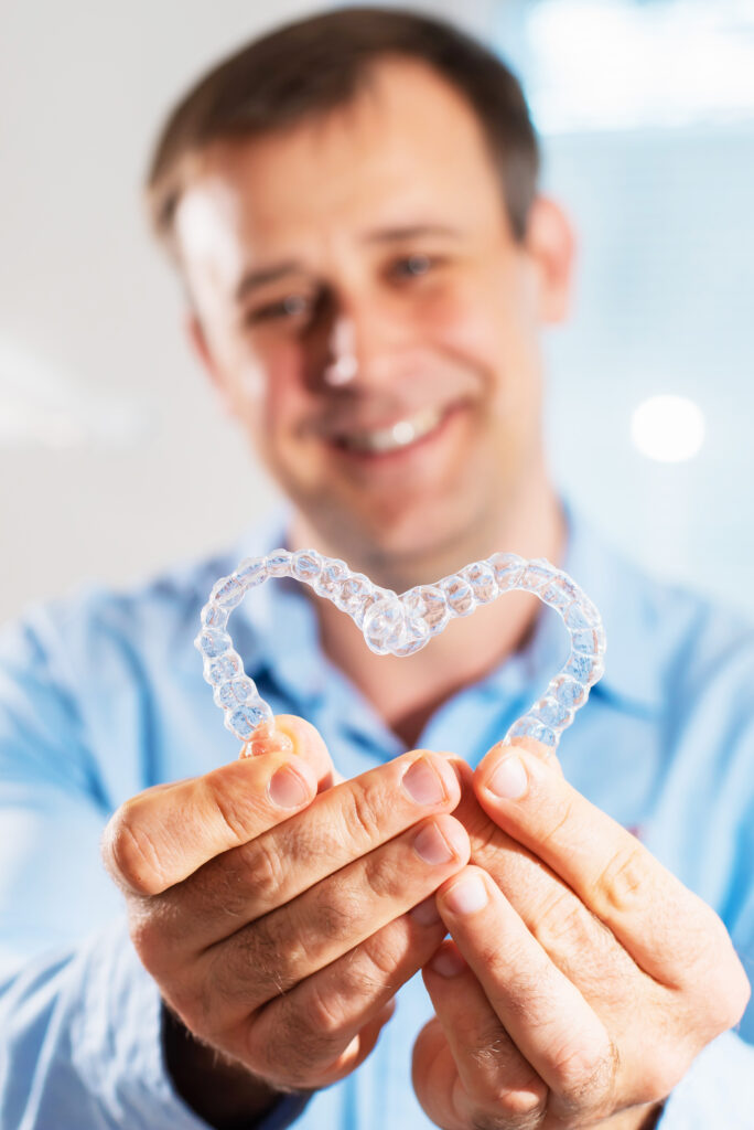 A man holding two Invisalign trays in the shape of a heart
