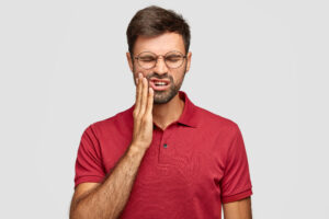 A man holds the side of his face due to tooth pain and a dental emergency.