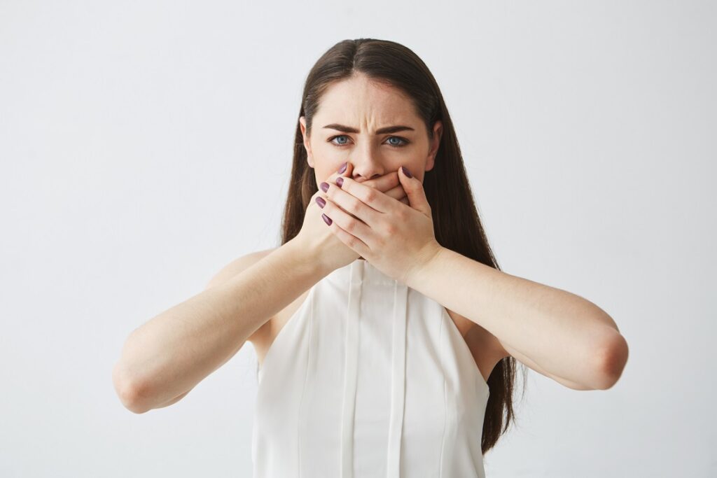 Young woman embarrassed about her bad breath, covering her mouth with both hands.