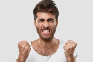Unshaven man clenches his teeth and balls his fists in frustration.