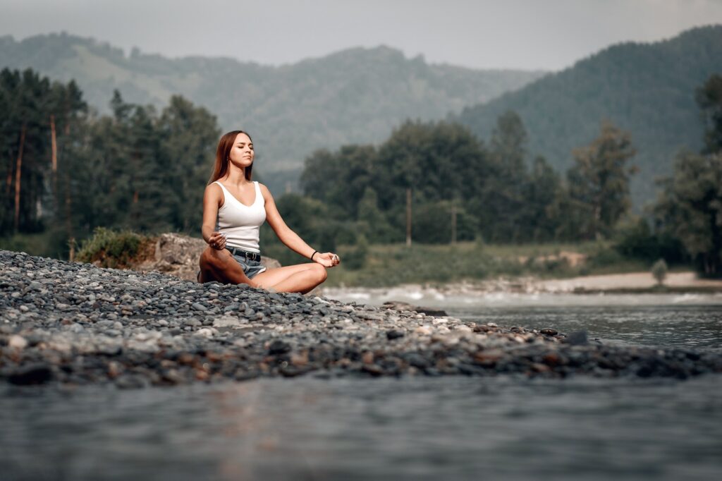 A young woman meditates in the wilderness beside a creek.