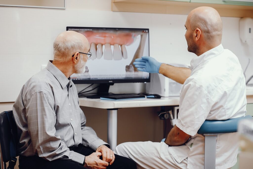 A male dentist shows an elderly male patient a photo of his teeth
