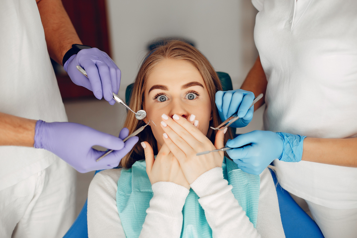 A young woman covers her mouth as dentists hold instruments to work on her teeth