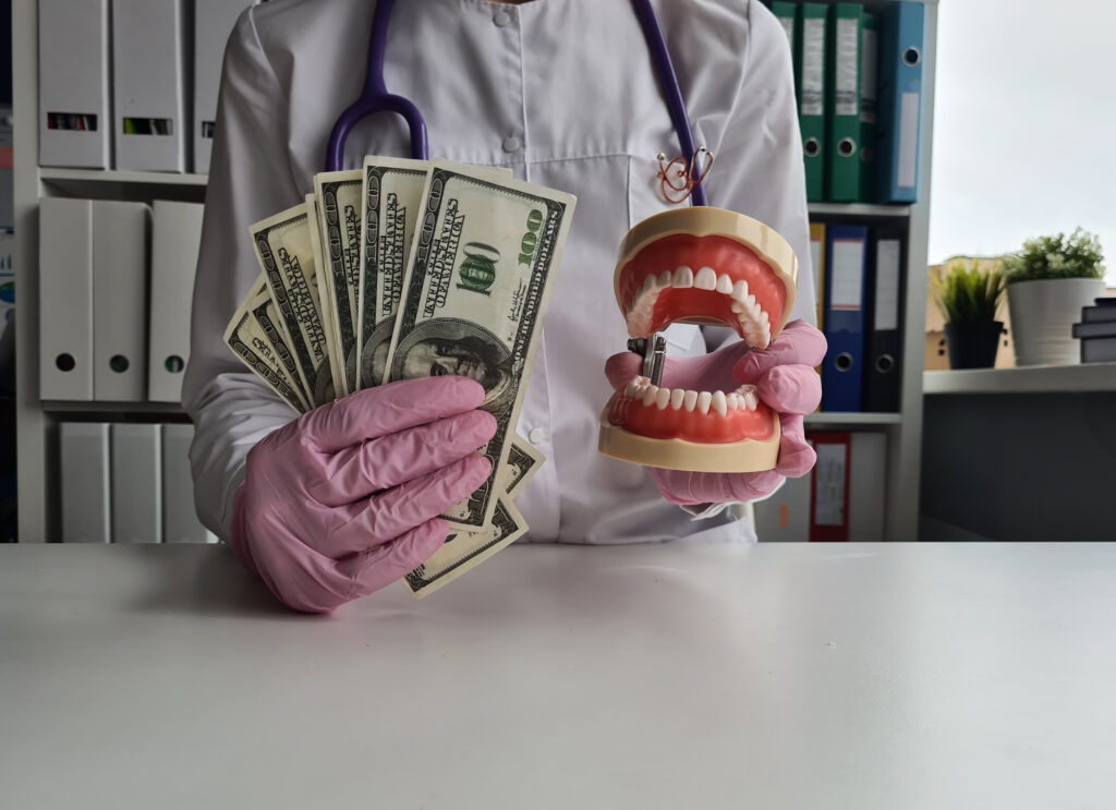 Expensive dental procedures can be burdensome - a dentist's gloved hand holds 100 dollar bills next to a denture.