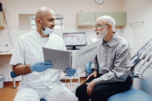 A dentist holding a treatment plan while explaining treatment to an elderly patient.