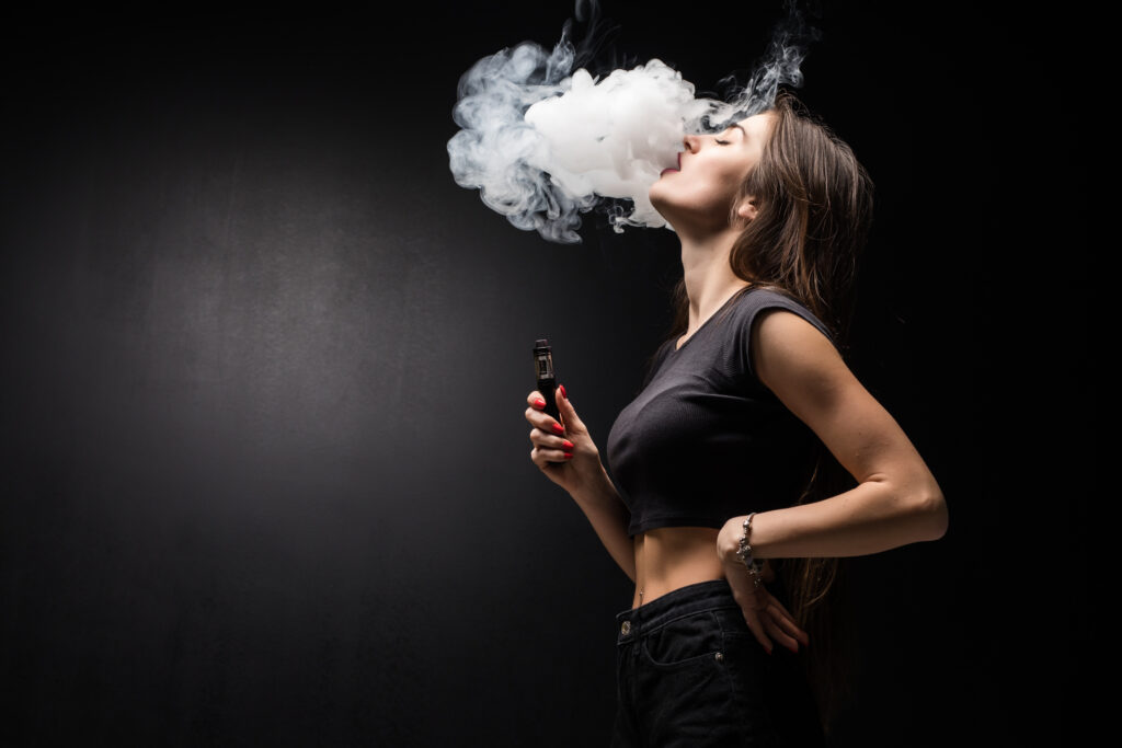 A young woman exhales smoke while holding a vape pen