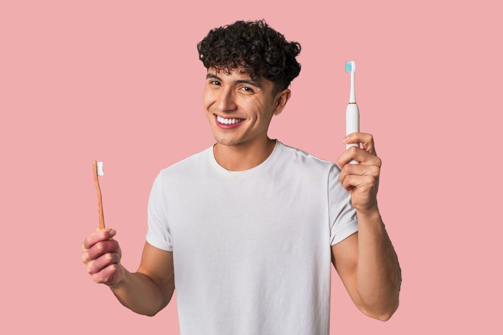 A young man holds an electric toothbrush above a manual toothbrush 