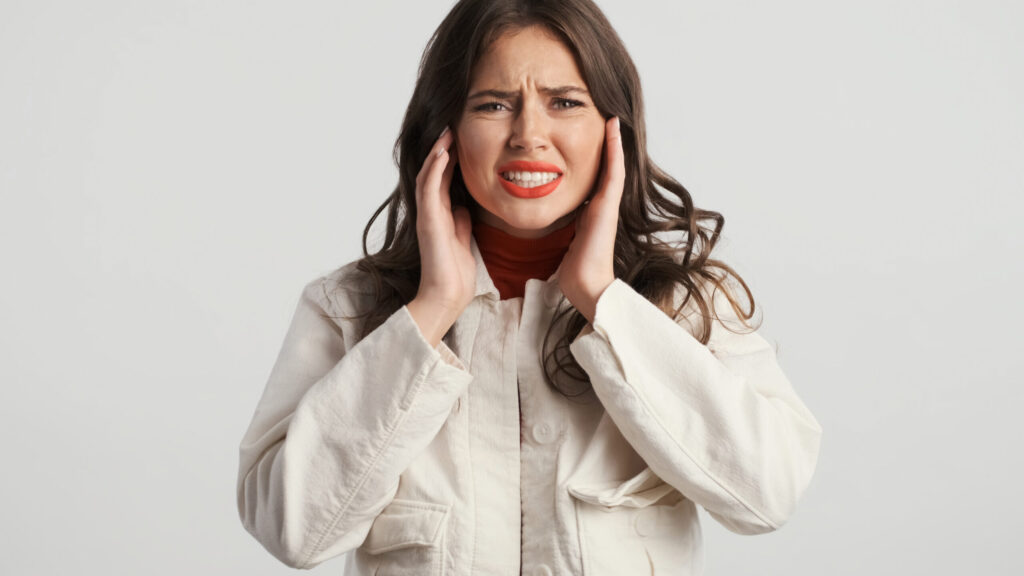 A woman with TMJ Disorder is shown holding her jaw joints and grimacing in pain