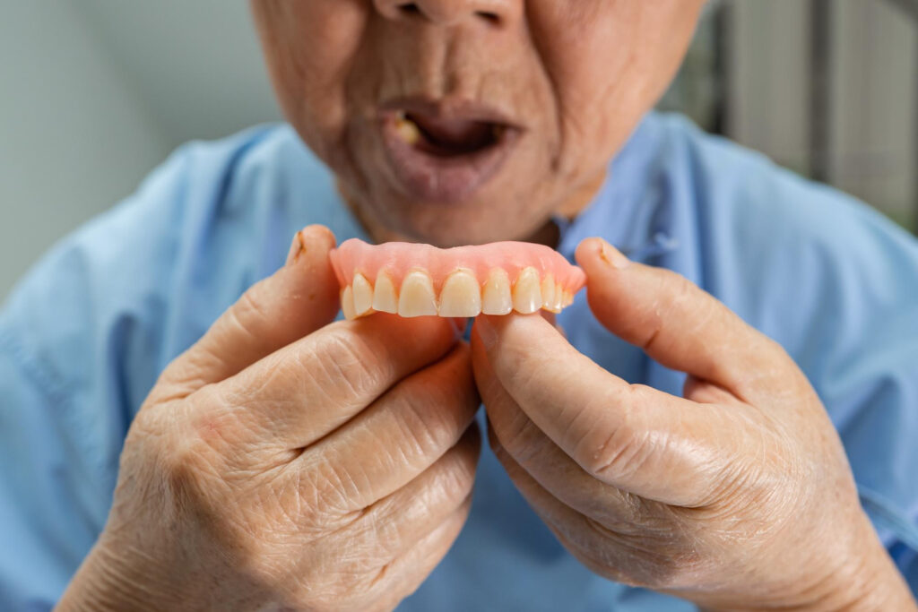 A senior holds his denture outside his mouth