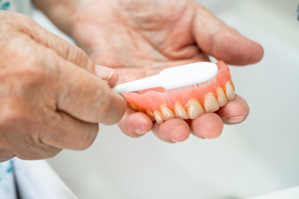 A person uses a soft brush to clean their denture