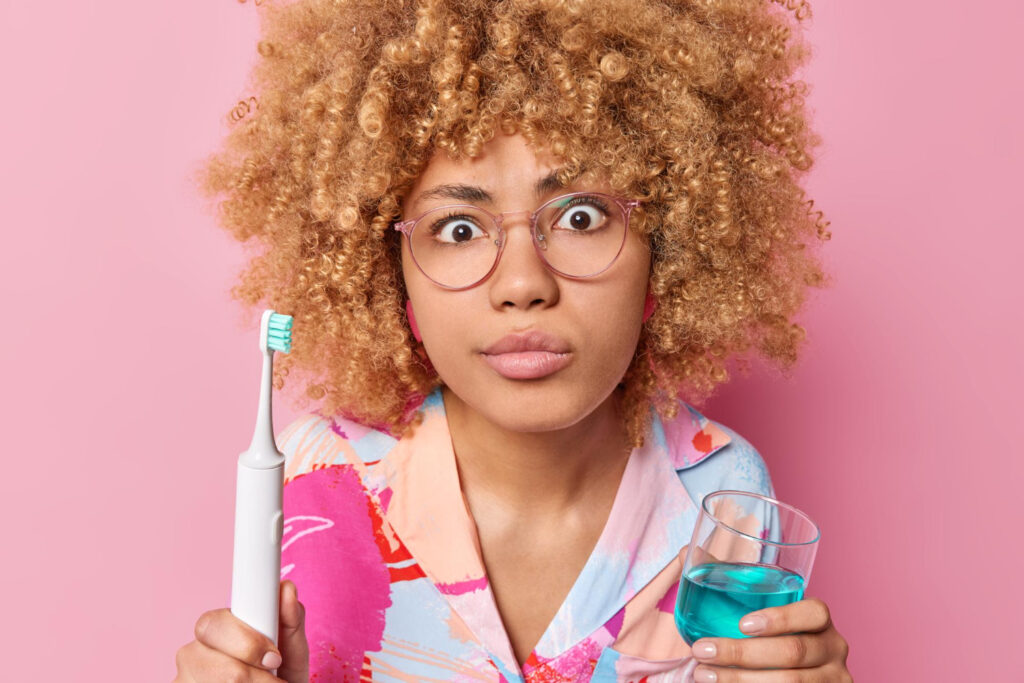 A woman holds a toothbrush and a glass of mouthwash