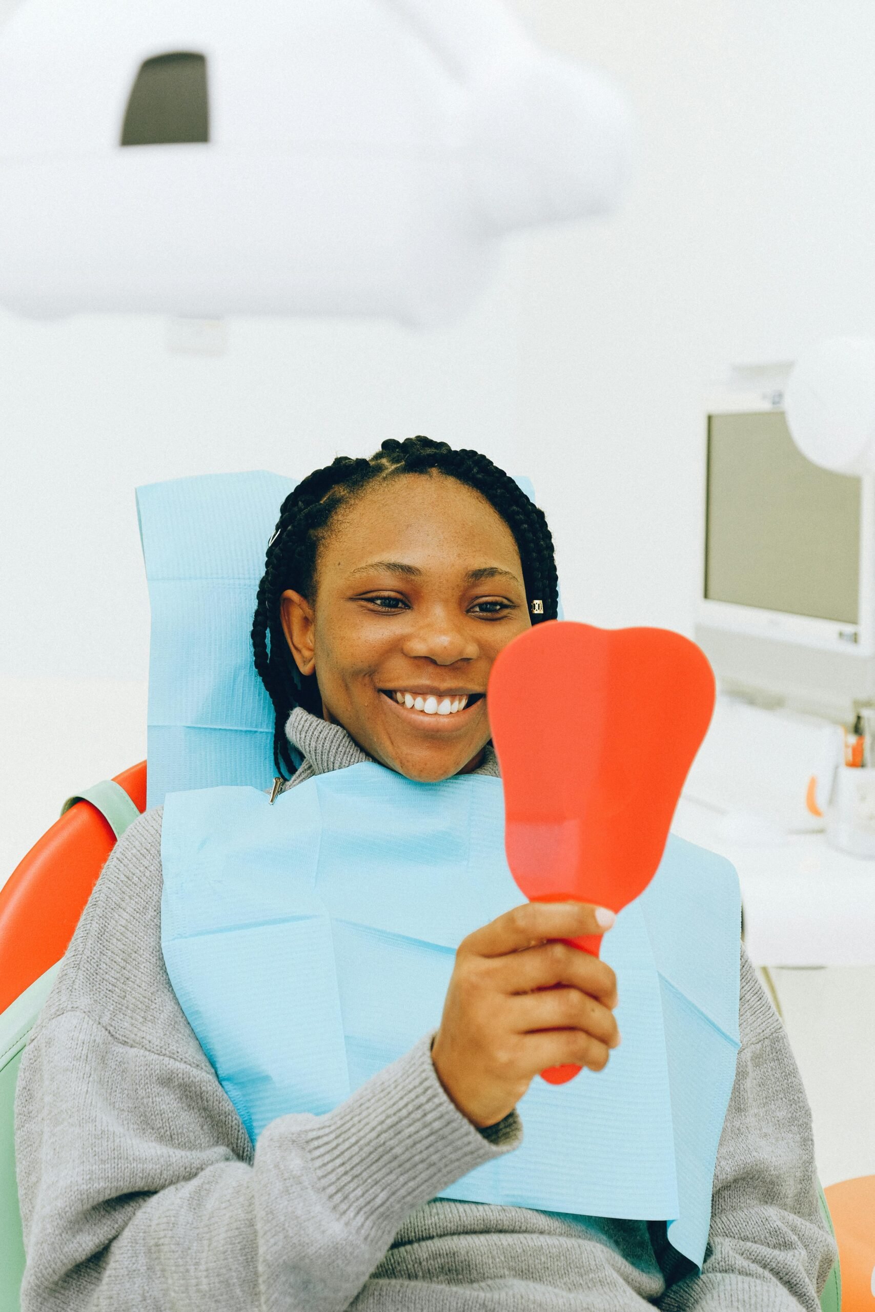 Patient in dental chair holding a tooth-shaped mirror.