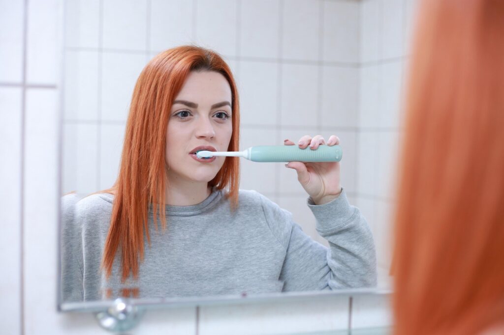 Person brushing teeth with an electric toothbrush in front of a mirror.