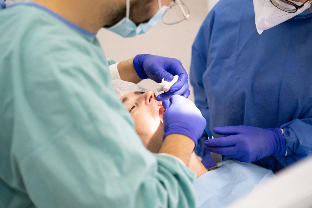 Dentists in protective gear working on a patient's teeth.