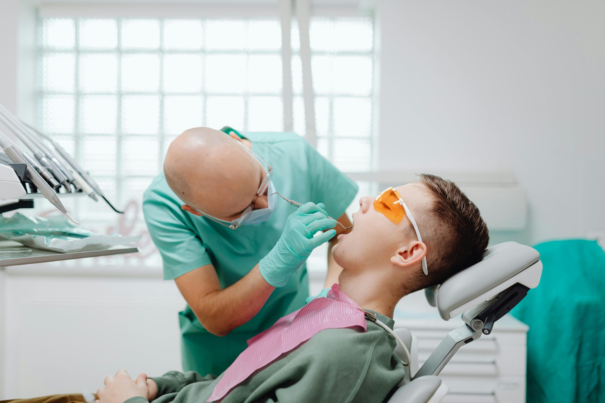 Dentist examining a patient wearing protective glasses in a dental chair.