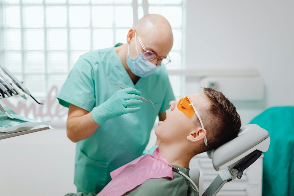Dentist in green scrubs examining a patient in a dental chair.