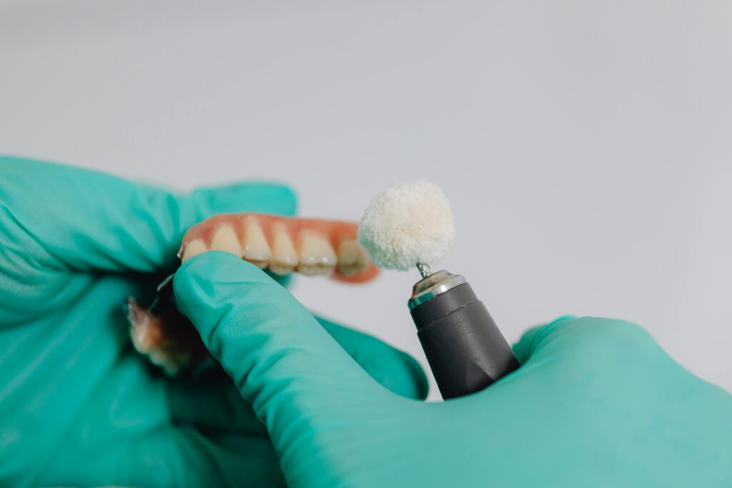 Gloved hands polishing dentures with a dental tool.