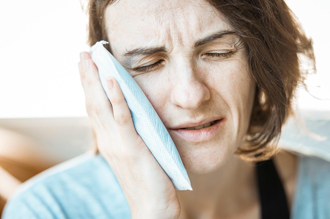 Person holding an ice pack to their cheek, appearing in pain.