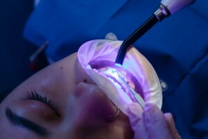 Dentist using a tool on metal braces in a patient's mouth.