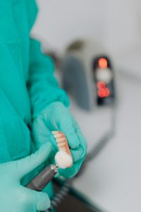 Gloved hands holding dentures with a dental tool for relining.