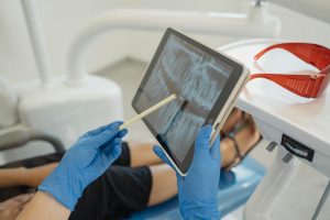 Dentist with gloved hands pointing at dental X-ray on tablet.