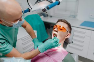 Dentist examining a patient wearing protective glasses in a dental chair.